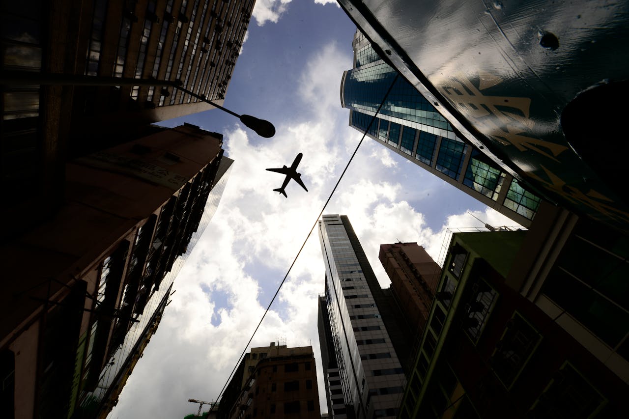 A commercial airplane flying above tall skyscrapers in a city, captured from a low-angle perspective against a bright sky, symbolizing the results of Managerial Bookkeeping